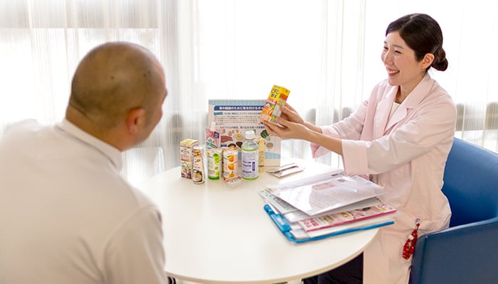 栄養士がパックの飲み物を手に取って笑顔で患者さんに栄養指導を行っている写真